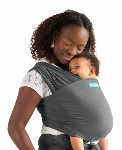 Woman holding a baby in a gray baby carrier against a white background. ELEMENTS SOFT & ADJUSTABLE FEATHER KNIT BABY WRAP CARRIER - 2 COLOURS | MOBY