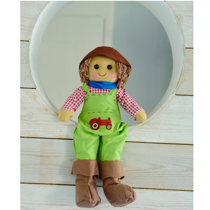 A ragdoll dressed as a farmer with green dungarees, red and white gingham shirt, blue neckerchief, brown hat, and boots. FARMER WEARING EMBROIDERED TRACTOR DUNGAREES RAGDOLL | POWELL CRAFT