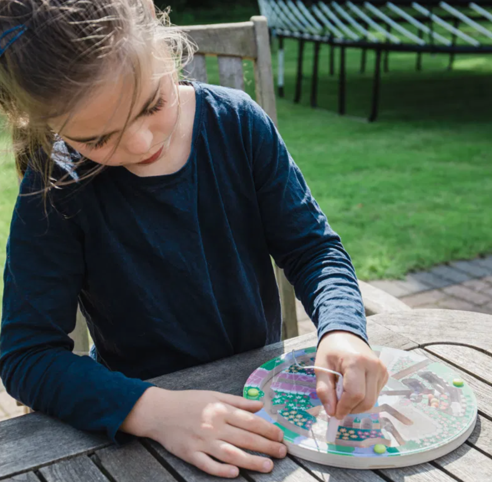 Child playing with a board game outdoors on a wooden table. FLOWER GARDEN MAZE PUZZLE GAME | BIGJIGS