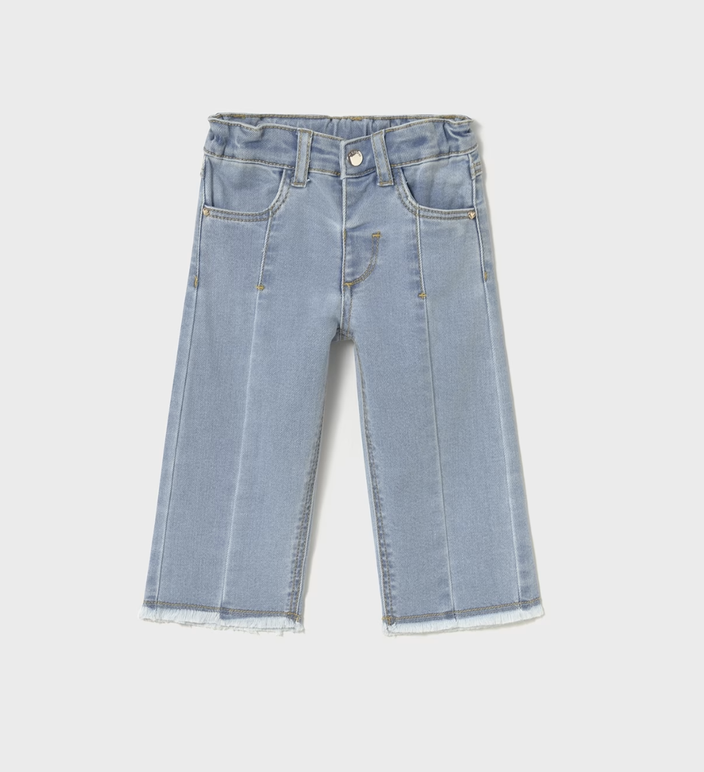 Full-length wide-leg flare jean in pale ice-blue or glacier wash stretch denim — clean, even, very light wash with a slight sheen; dramatically wide sweeping flare from the knee downward in a strong 70s-inspired wide-leg silhouette; prominent vertical centre-front pressed crease line running the full length of each leg from the hip to the hem; structured centre-front waistband panel with a small round silver metal snap-stud fastening at the top centre; two small angled front hip pockets; golden or mustard-y