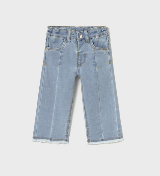 Full-length wide-leg flare jean in pale ice-blue or glacier wash stretch denim — clean, even, very light wash with a slight sheen; dramatically wide sweeping flare from the knee downward in a strong 70s-inspired wide-leg silhouette; prominent vertical centre-front pressed crease line running the full length of each leg from the hip to the hem; structured centre-front waistband panel with a small round silver metal snap-stud fastening at the top centre; two small angled front hip pockets; golden or mustard-y