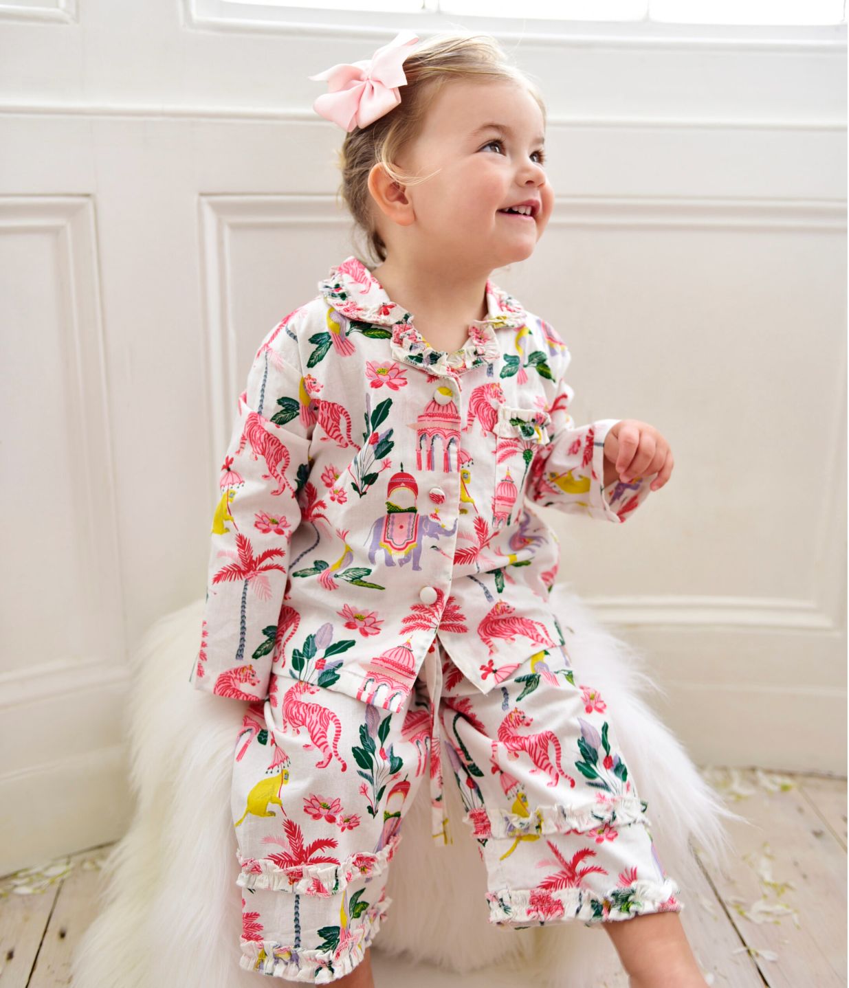 Child in a floral outfit with a pink bow, standing indoors. GIRL'S SULTAN'S GARDEN LONG COTTON PYJAMAS - 3 SIZES | POWELL CRAFT