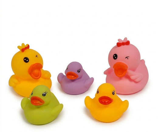 Snuggle Baby Family of Ducks Bath Toys set of five colourful vinyl rubber ducks shown on a white background; two larger parent ducks — one sunshine-yellow with a small orange crown and one bright pink with a small red bow — and three smaller ducklings in lime or apple-green, soft lavender-purple and golden yellow; all five have rounded squeaky-duck bodies with small wing stubs, orange beaks and cartoon eyes with lashes; arranged in a loose group facing slightly different directions