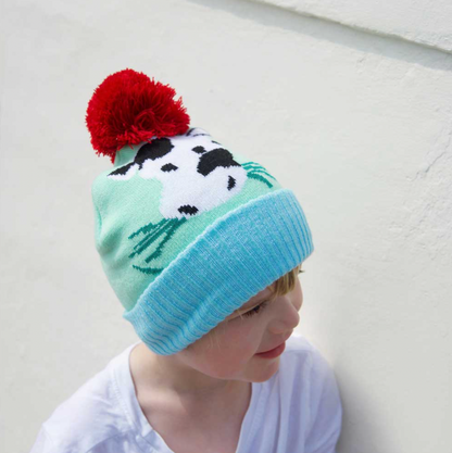 Child wearing a colorful knit hat with a red pom-pom. KID'S COW FARMYARD KNIT HAT WIHT POM-POM | POWELL CRAFT