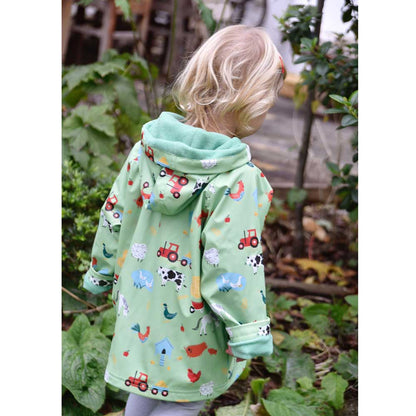 Child wearing a green raincoat with farm animal prints, standing in a garden. KID'S FARMYARD LINED RAINCOAT - 4 SIZES | POWELL CRAFT