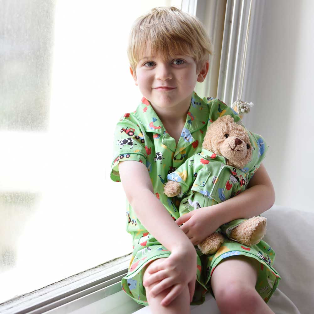 Child in green pajamas holding a teddy bear by a window. KID'S FARMYARD SHORTS & TOP PYJAMA SET - 3 SIZES | POWELL CRAFT