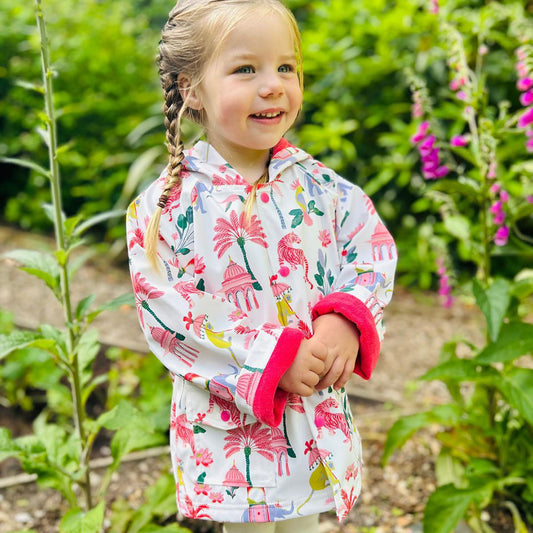 Young girl in a floral raincoat standing in a garden. KID'S SULTAN'S GARDEN LINED RAINCOAT - 3 SIZES | POWELL CRAFT