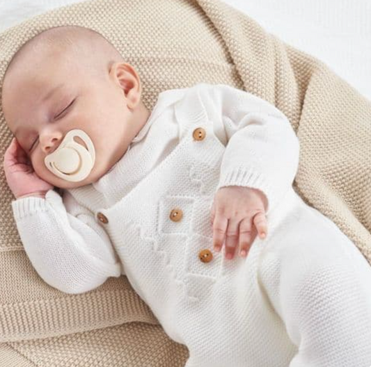 Baby sleeping peacefully wearing a white outfit with buttons on a beige blanket. KNITTED BABY DUNGAREE & TOP - WHITE | DANDELION