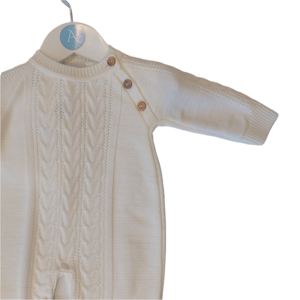 Upper body of the white knitted onesie on an Annabel's of Cranbrook branded hanger; central cable-knit chest panel, smoother knit side panels, and three round wooden shoulder buttons visible