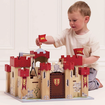 Child playing with a wooden toy castle on a white background. LIONHEART WOODEN TOY CASTLE | LE TOY VAN