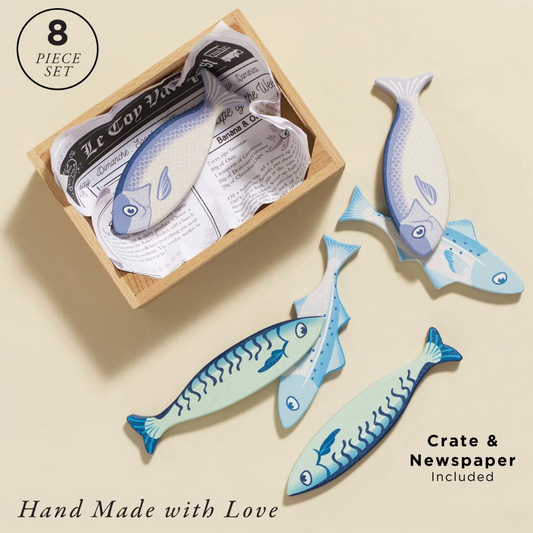 Set of four blue fish-shaped napkin holders with a cardboard box labeled 'Crate & Newspaper' on a beige background. MARKET FISH WOODEN TOY CRATE | LE TOY VAN