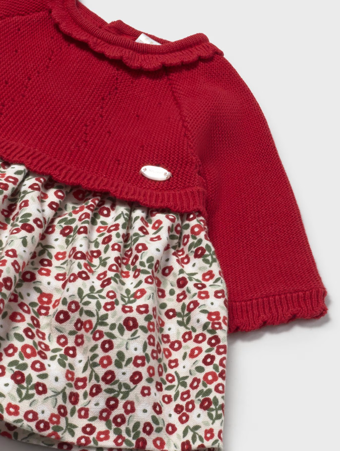 Close-up — knit texture vs woven floral contrast; scalloped neckline edge; silver badge; fabric transition point; pointelle detail. 