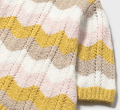 Mayoral Baby Girl Autumn Wave Knitted Dress — close-up detail shot on light grey background; cropped view of the dress body and right sleeve showing the all-over chevron wave knit pattern in close detail; mustard yellow, pale pink, soft taupe and cream wave bands clearly visible with raised textured wave knit stitch; vertical ladder-stitch detailing between the wave bands adds depth and texture; mustard yellow ribbed cuff at the wrist visible at the bottom right; light grey background; demonstrates the qual