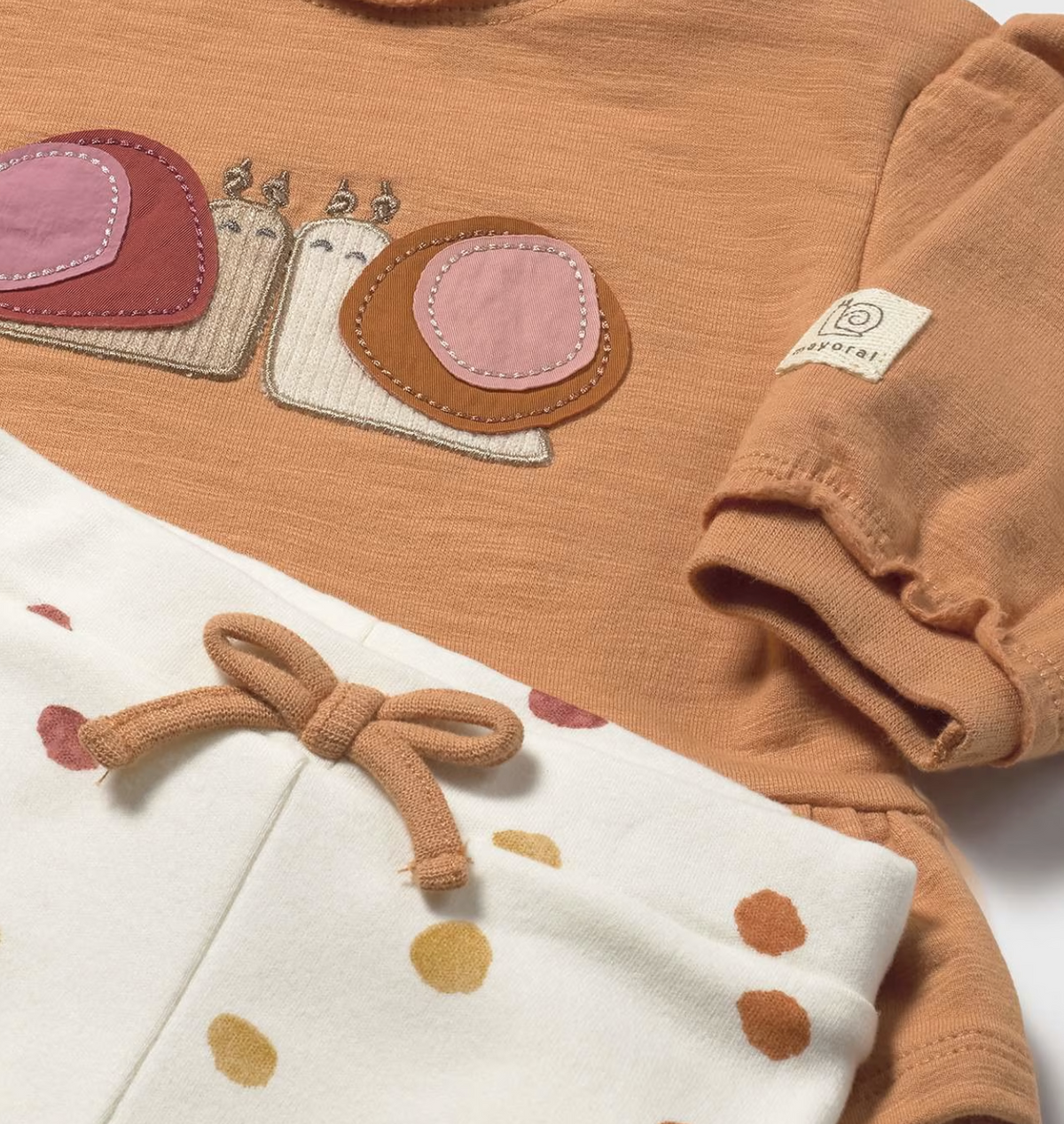 Close-up — snail appliqué detail; cream ribbed bodies; raspberry and cinnamon shells; white blanket stitch; Mayoral label; bow at waistband. 