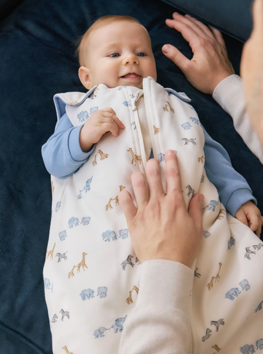 Lifestyle — very young baby on dark navy; pale blue bodysuit coordinating with bluebell lining; parent's hands; intimate setting.