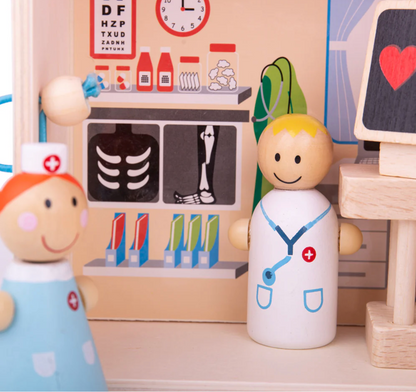 Wooden toys of a doctor and a nurse in a playroom setting with medical-themed decorations. MINI WOODEN HOSPITAL PLAYSET | BIGJIGS