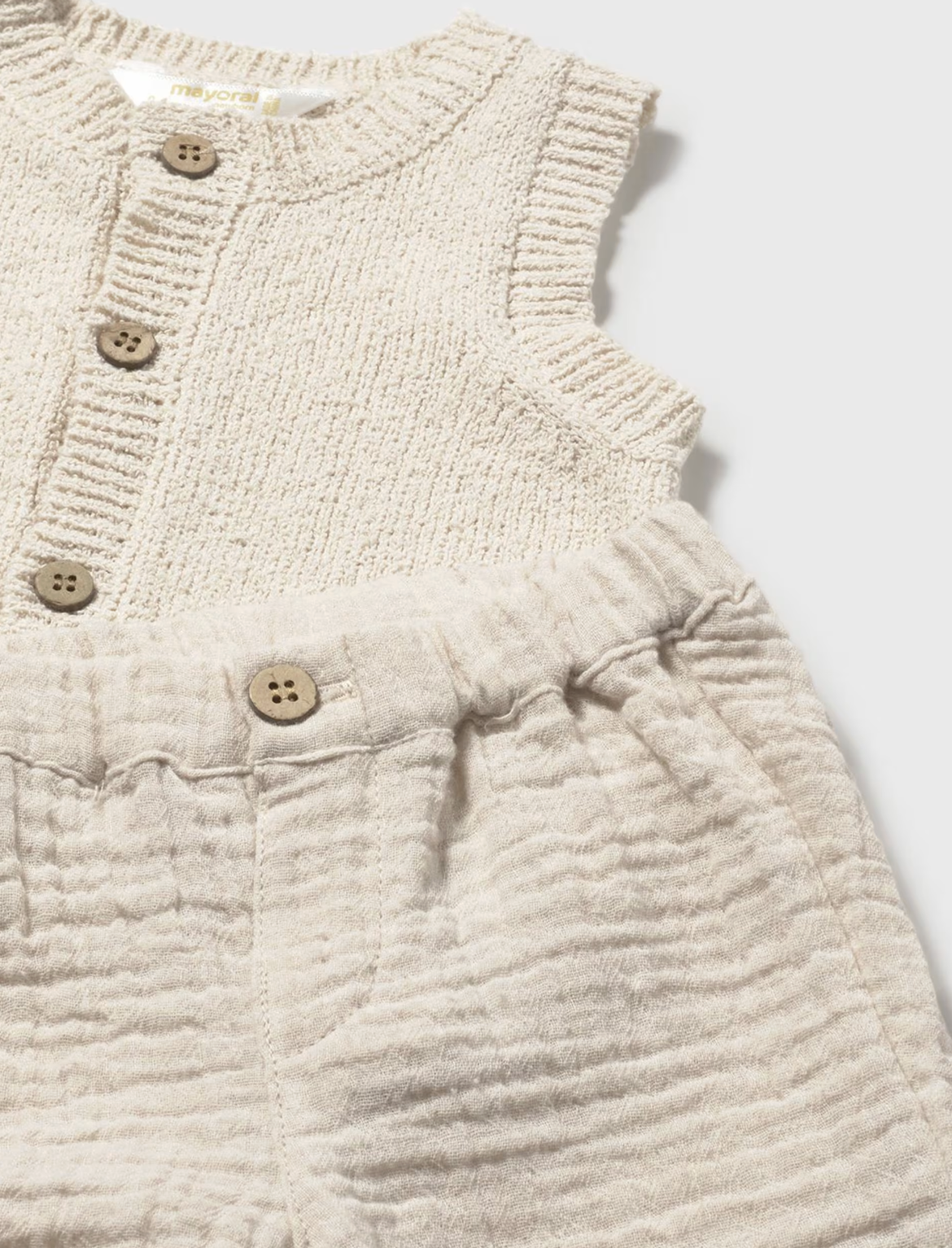 Close-up of a textured beige sleeveless garment with button details. NEUTRAL BABY SHORTS WITH VEST AND T-SHIRT SET | MAYORAL