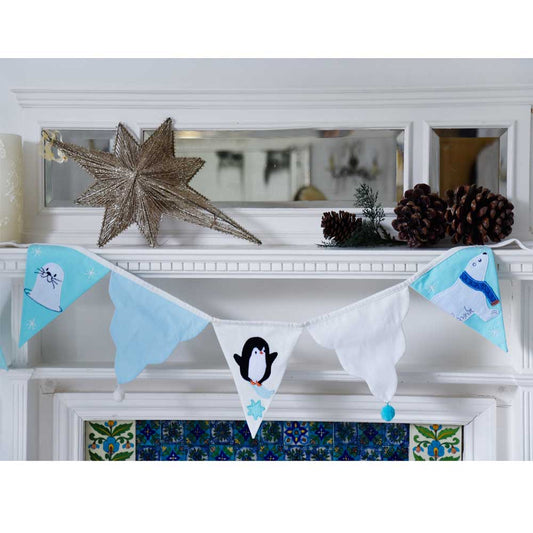Polar bear and penguin-themed banner on a fireplace mantel with decorative items. POLAR BEAR & PENGUIN WITH POM POMS BUNTING FOR BEDROOMS & PARTIES | POWELL CRAFT