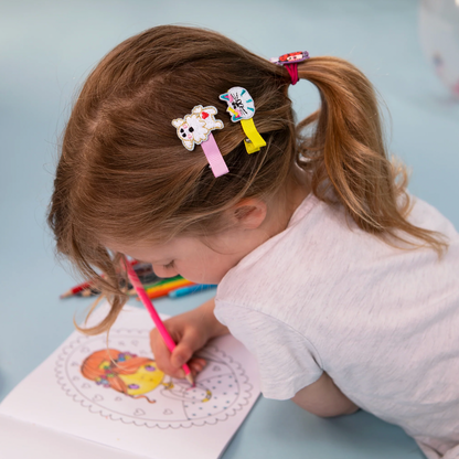 Child with hair clips coloring a picture on a light blue background. RACHEL ELLEN HAIR CLIPS - DOGS
