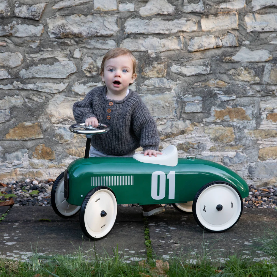 Child sitting in a green toy car with '01' on a stone wall background. RIDE ON CLASSIC CAR - BRITISH RACING GREEN WITH WHITE SEAT | VILAC 