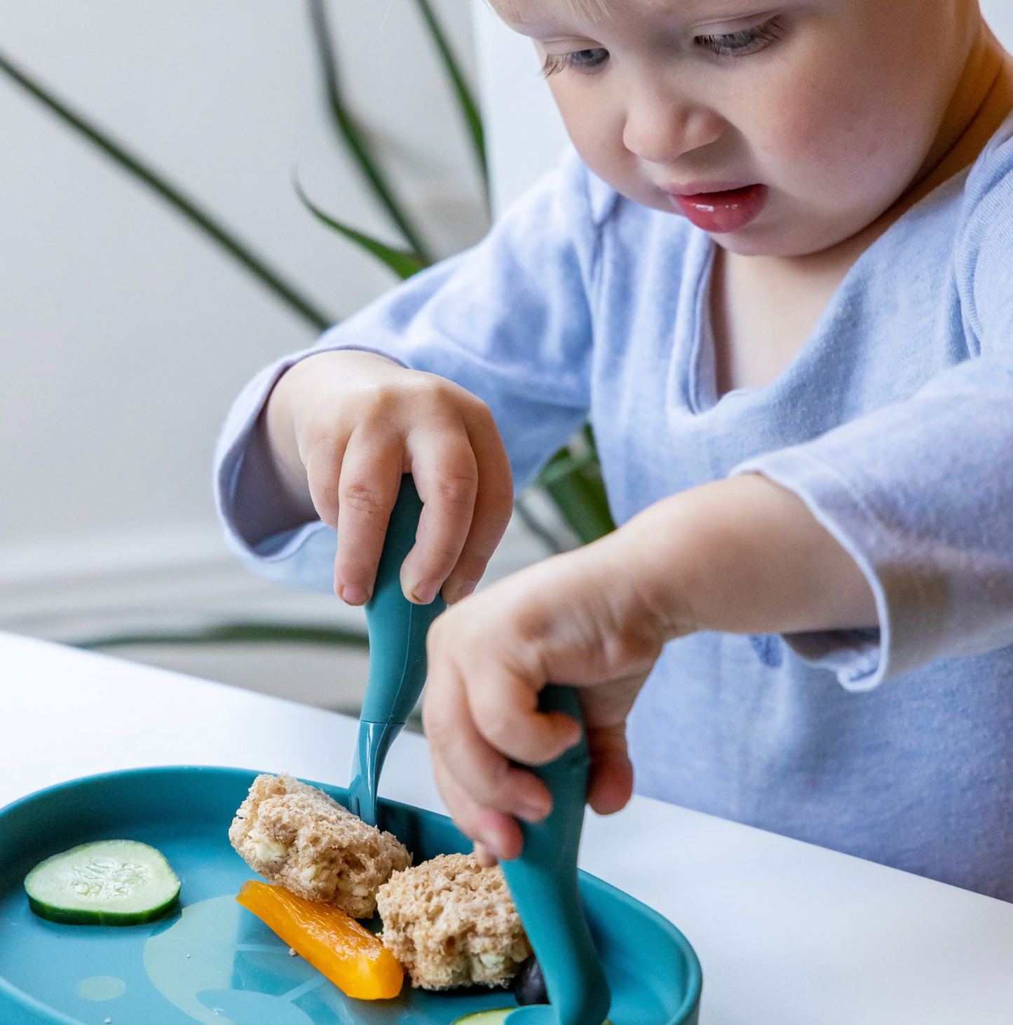 Child using blue utensils to eat rice cakes and vegetables on a plate. SILICONE BABY TRAVEL CUTLERY SET WITH CASE - 2 COLOURS | TUM TUM