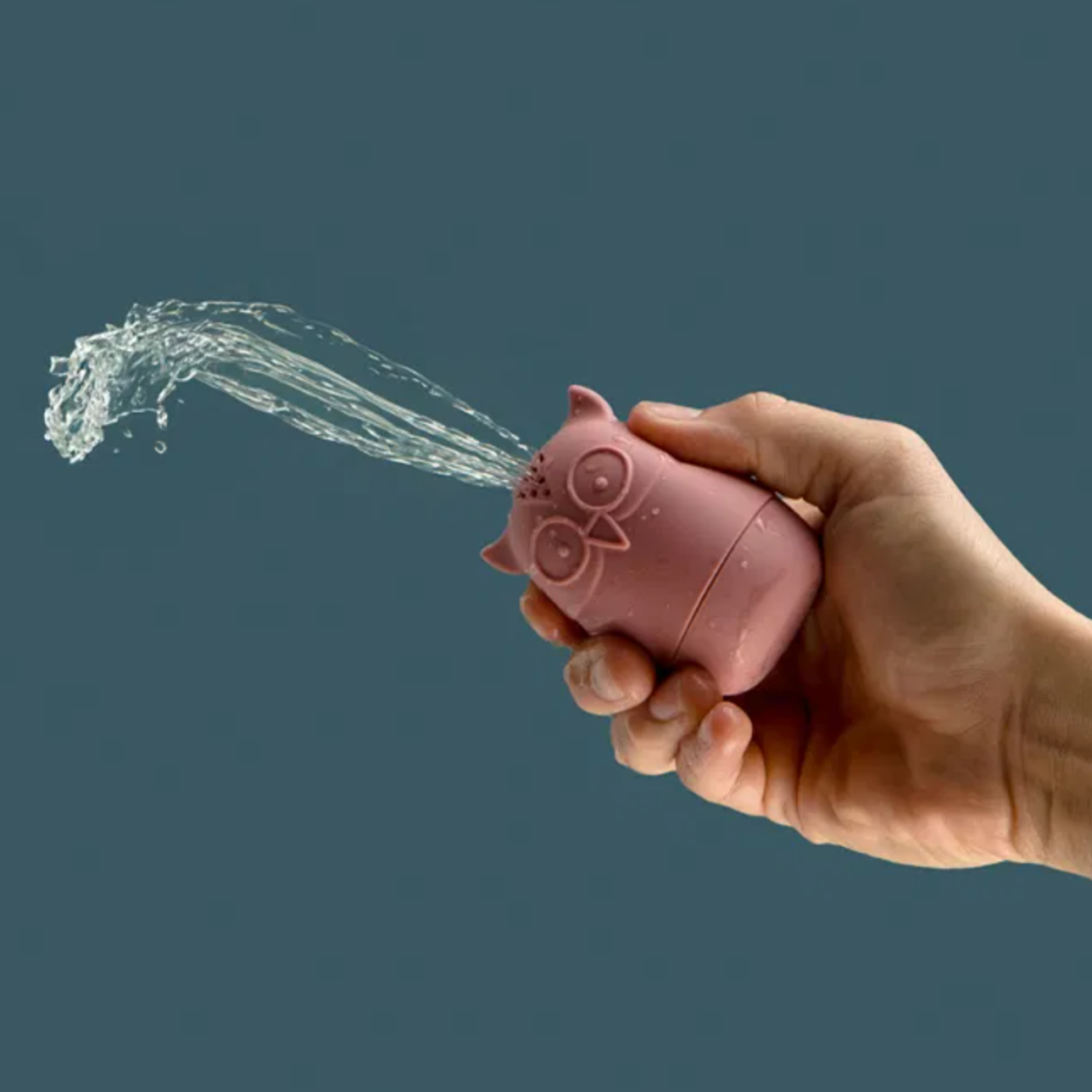 Hand holding a pink water gun with water being sprayed against a dark background SILICONE BATH ANIMALS | BIGJIGS
