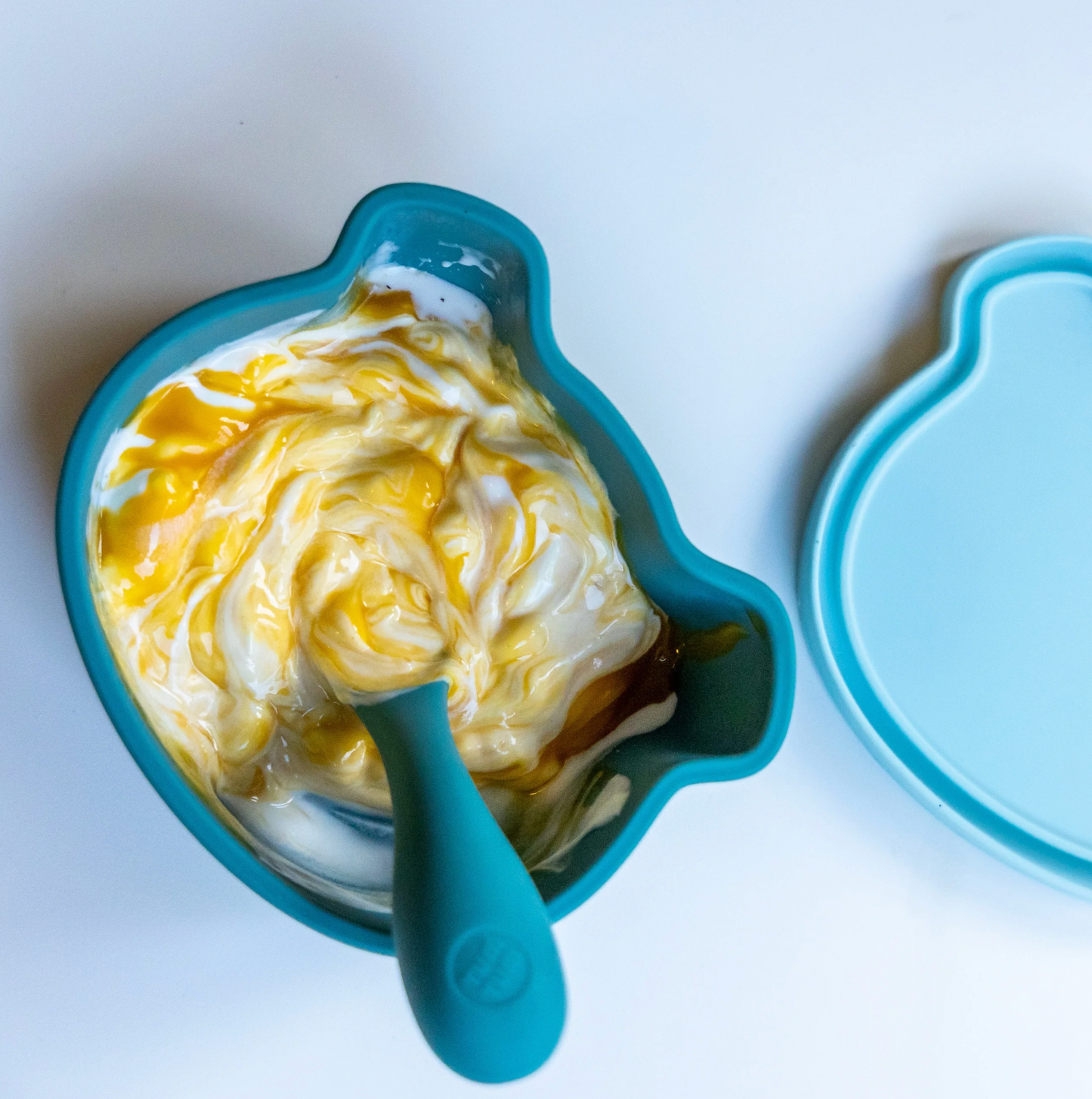 Blue bowl with swirled food and matching spoon. SILICONE TRAVEL WEANING BOWL & SPOON SET - 2 COLOURS | TUM TUM 