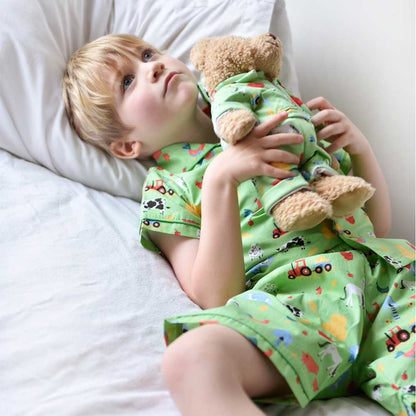 Child in colorful pajamas holding a MATCHING teddy bear on a bed. KID'S FARMYARD SHORTS & TOP PYJAMA SET - 3 SIZES | POWELL CRAFT