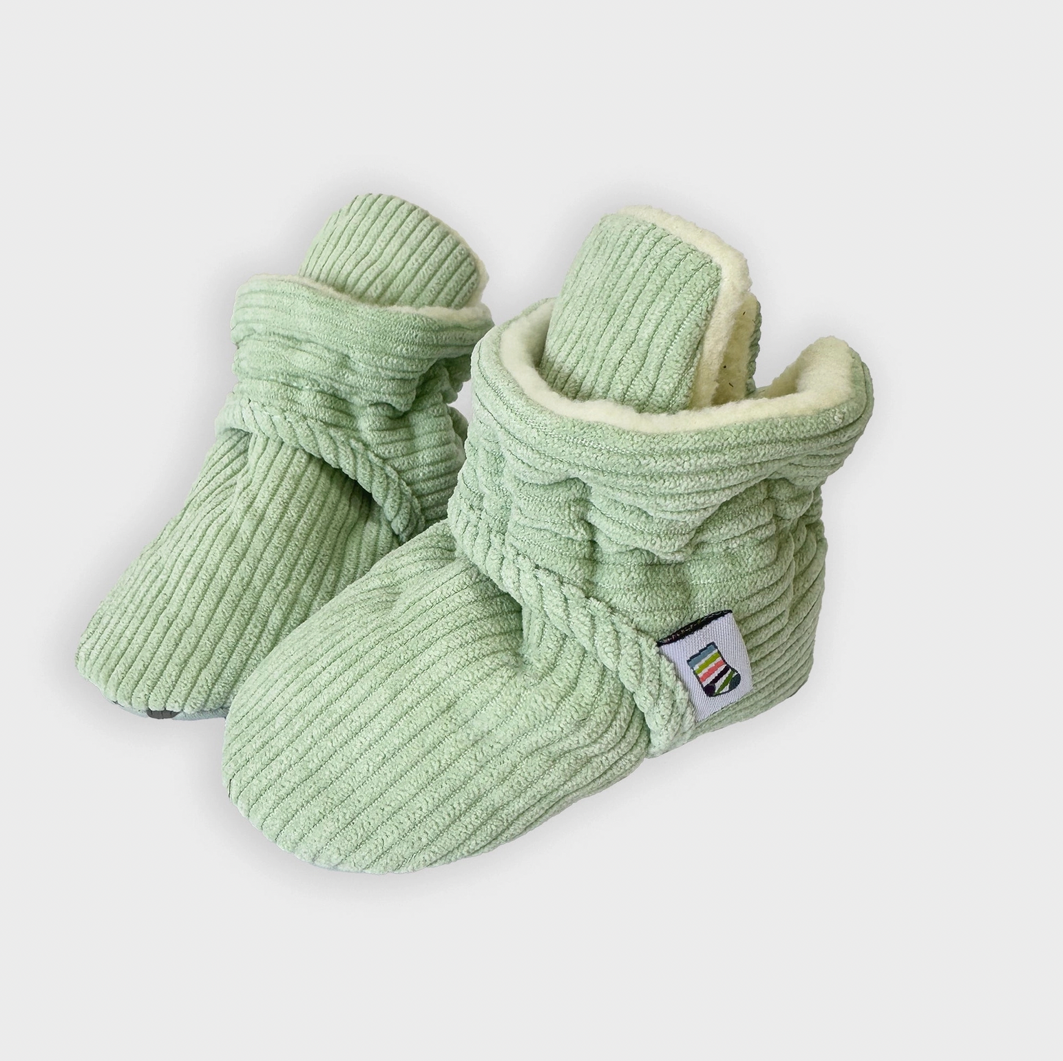 Pair of green baby booties with a textured pattern on a white background STAY-ON, NON-SLIP BOOTIE - PISTACHIO CORDUROY | THE LITTLE SOCK CO.