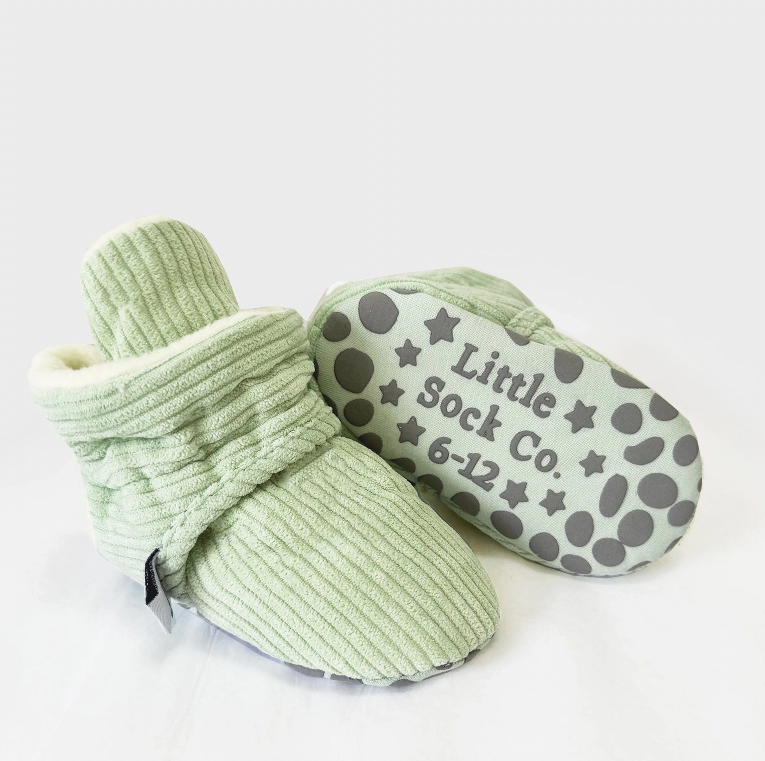 Pair of green baby booties with patterned sole on a white background STAY-ON, NON-SLIP BOOTIE - PISTACHIO CORDUROY | THE LITTLE SOCK CO.