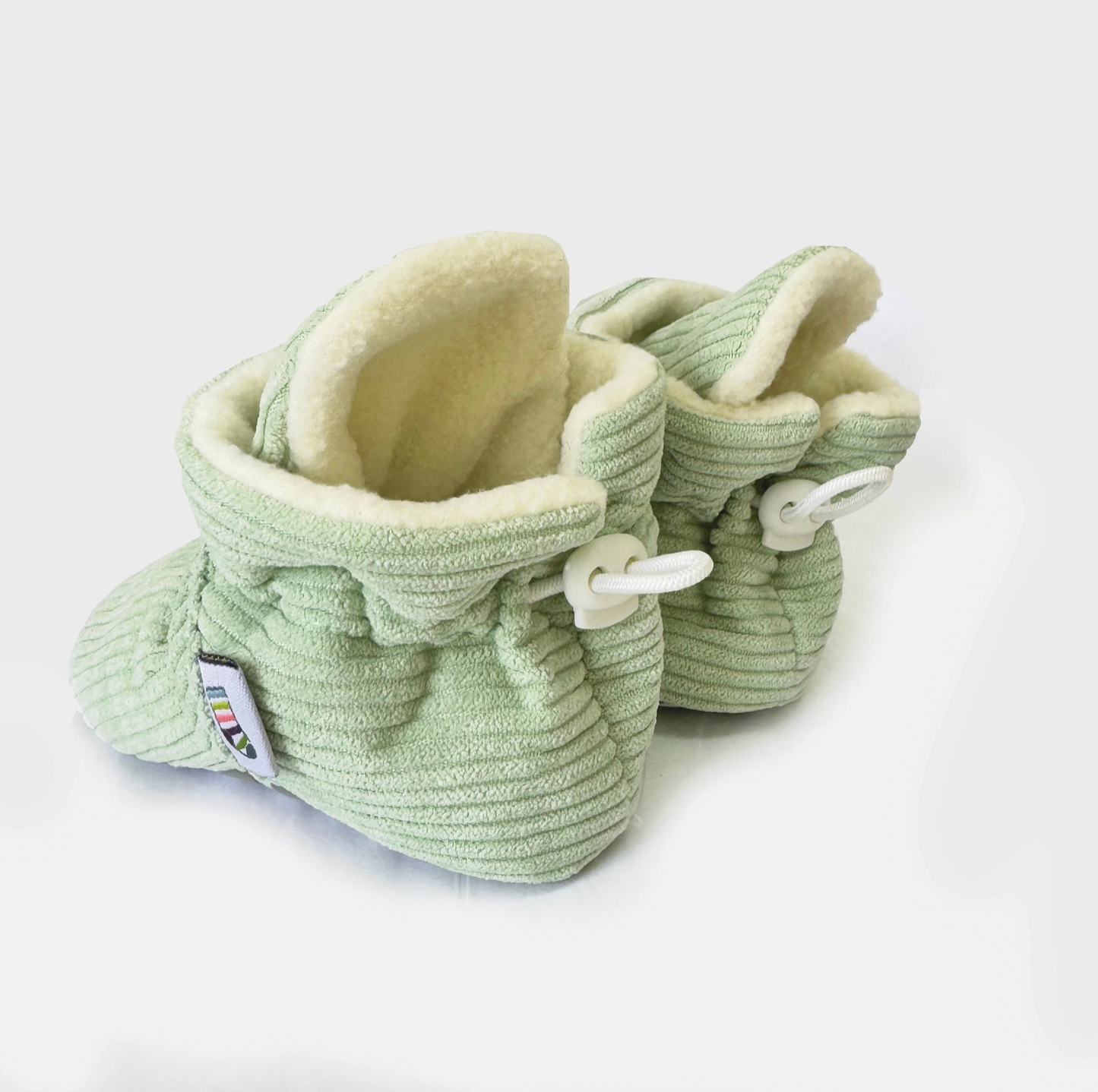 Pair of light green baby booties with white laces on a white background STAY-ON, NON-SLIP BOOTIE - PISTACHIO CORDUROY | THE LITTLE SOCK CO.