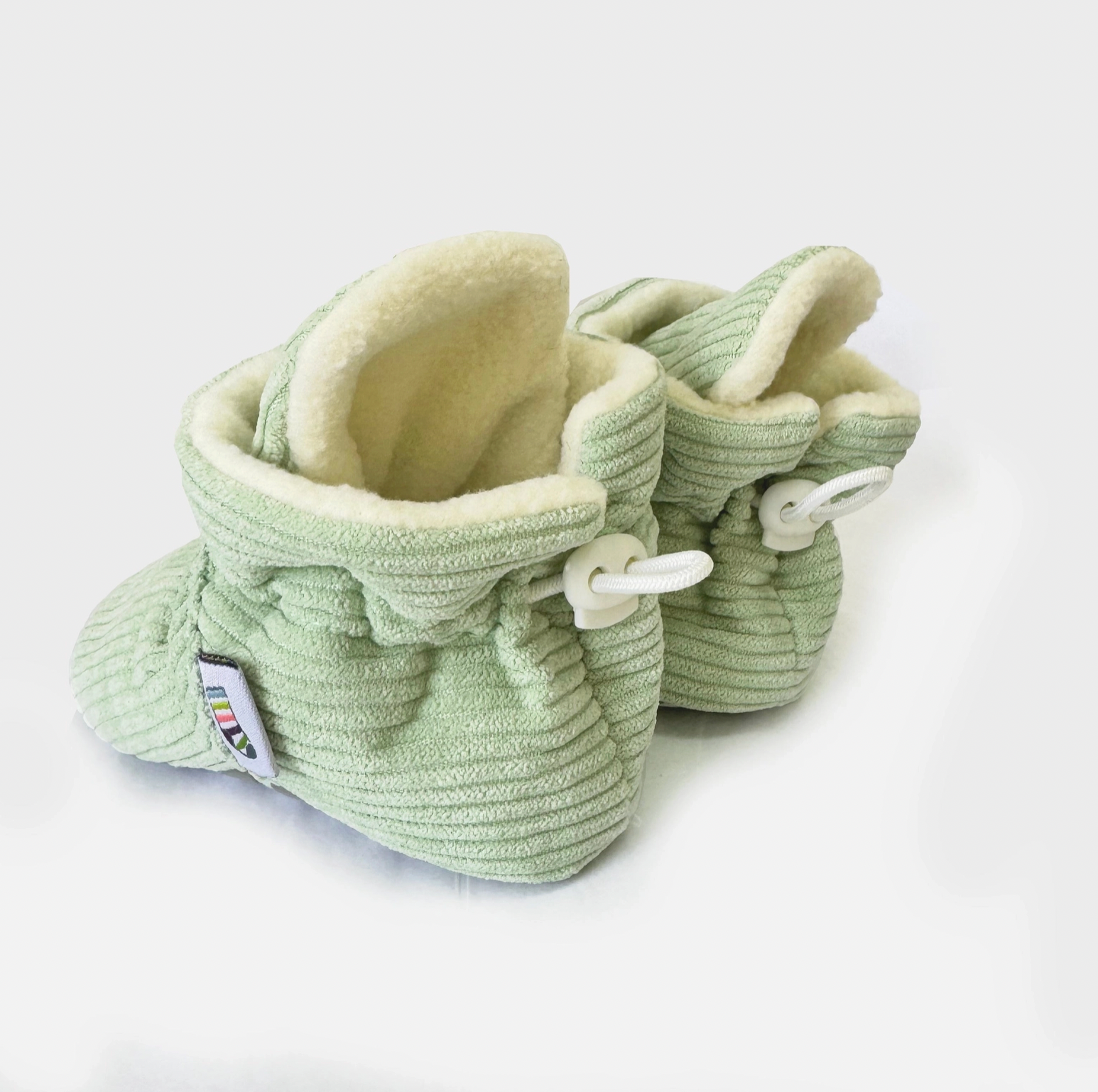 Pair of light green baby booties with white laces on a white background STAY-ON, NON-SLIP BOOTIE - PISTACHIO CORDUROY | THE LITTLE SOCK CO.