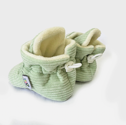 Pair of light green baby booties with white laces on a white background STAY-ON, NON-SLIP BOOTIE - PISTACHIO CORDUROY | THE LITTLE SOCK CO.