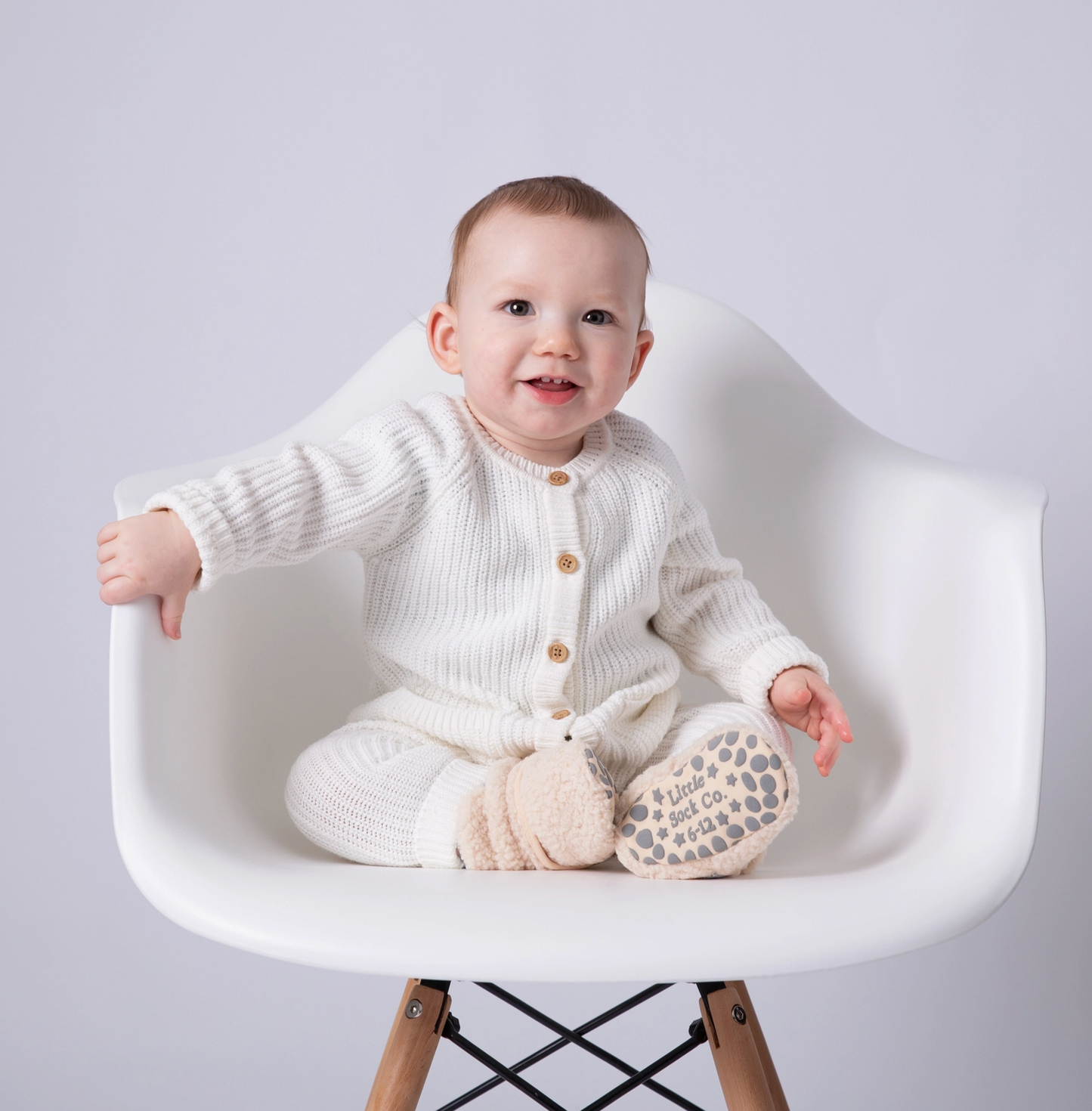 Baby in a white knit outfit sitting on a white chair with a plain background STAY-ON, NON-SLIP BOOTIE - SHERPA | THE LITTLE SOCK CO.