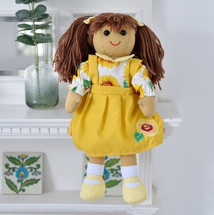 A brown-haired ragdoll wearing a yellow pinafore dress with a sunflower design, yellow gingham shoes, and a sunflower-themed shirt. SUNFLOWER RAGDOLL WITH BROWN HAIR AND PINAFORE DRESS | POWELL CRAFT