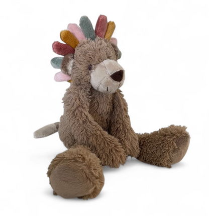A plush stuffed animal shaped like a small brown bear or lion sitting on a white background, with a soft gray snout and feet, brown body, and a colorful spiky mane in muted pink, blue, green, yellow, and brown.