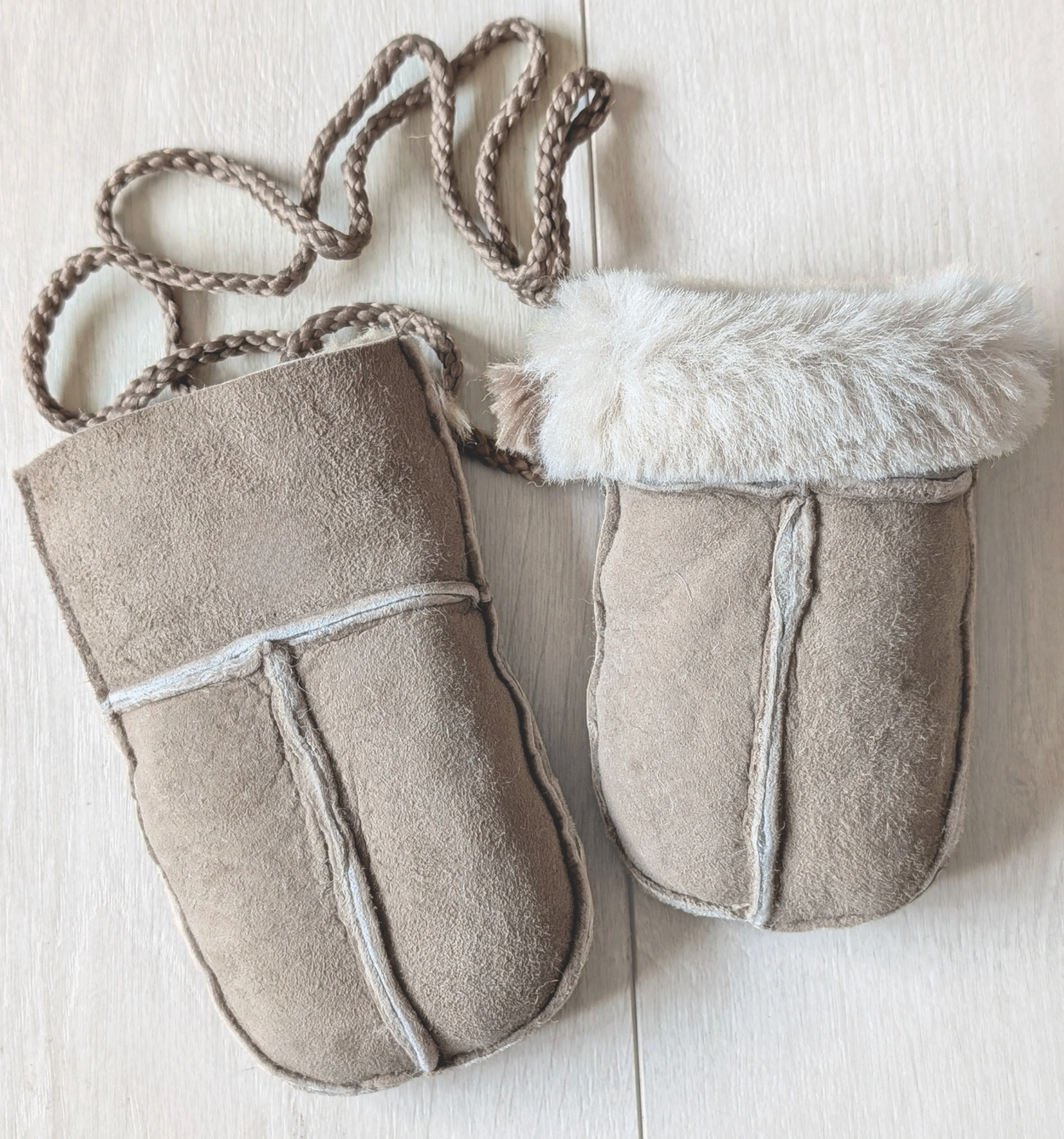 A pair of beige suede pouches with white faux fur trim and braided rope handles, laid flat on a light wood background.