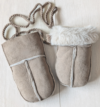 A pair of beige suede pouches with white faux fur trim and braided rope handles, laid flat on a light wood background.