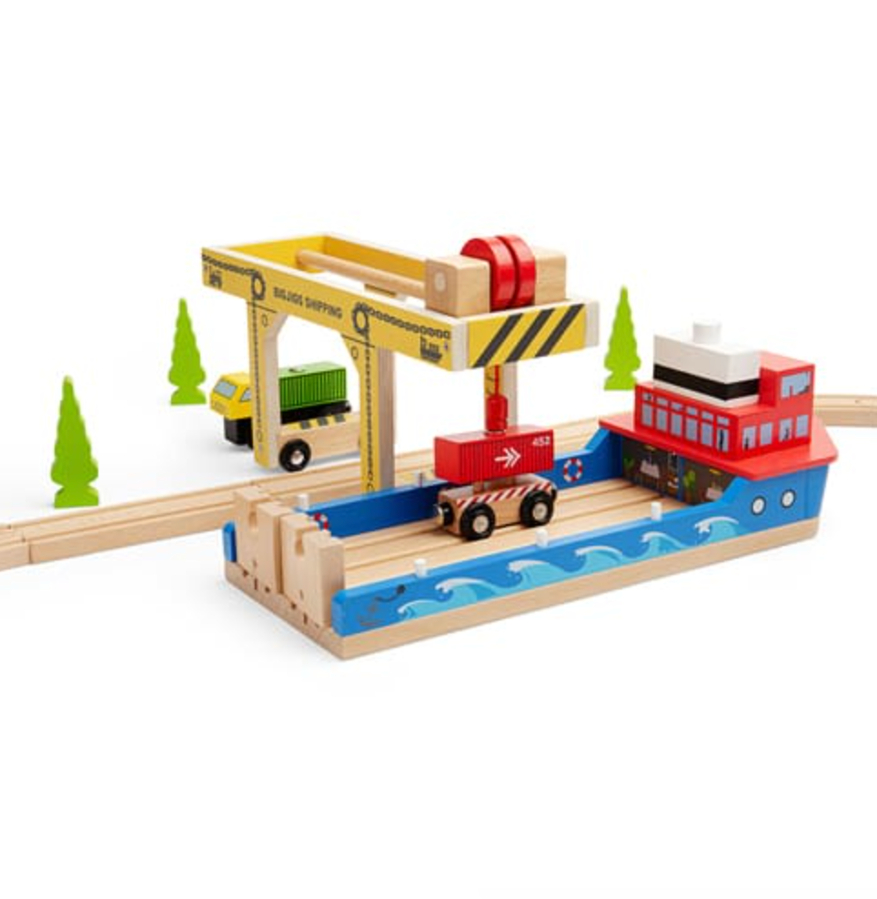A wooden toy port and cargo train set on a white background, featuring a blue boat with a red cabin, a yellow crane, a small green truck, and green trees.