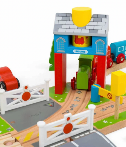 A colorful wooden toy train set with a small green train under a blue and red station-like house, wooden tracks, white fences, a red car, and a blue train on a white background.