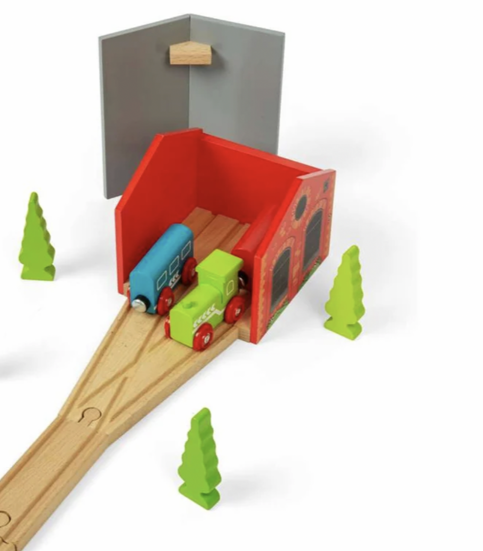 A wooden toy train set with a red train shed, light wood tracks, two colorful toy trains, and small green tree shapes on a white background.