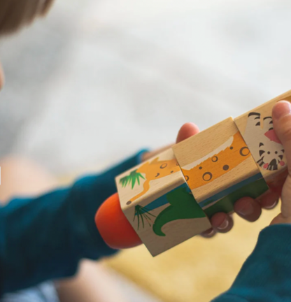 A close-up of a child's hands holding a wooden animal puzzle toy with painted safari designs, including a giraffe, crocodile, and tiger, with a bright orange piece visible.