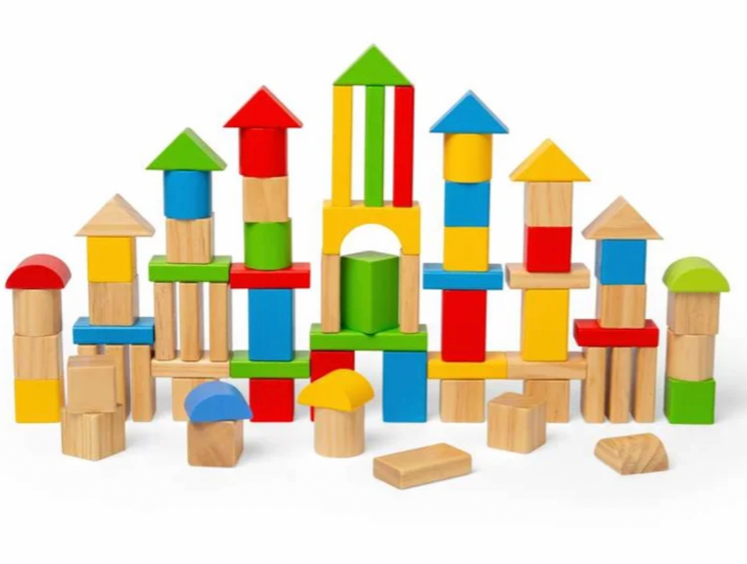 A set of colorful wooden building blocks arranged to form small towers, houses, and arches on a plain white background.