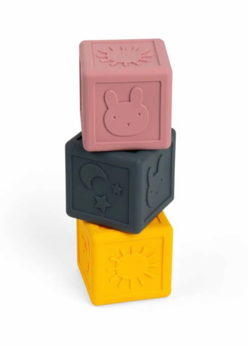 Three stacked silicone baby blocks in dusty pink, dark gray, and mustard yellow, each featuring embossed animal and sun motifs, on a white background.