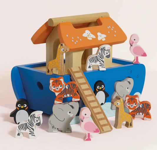 A wooden Noah's Ark toy set with a blue ark, orange roof, ladder, and painted animal figures including giraffes, zebras, tigers, penguins, elephants, flamingos, and a pink flamingo on a light beige background.