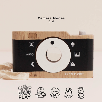 LE TOY VAN W/2R wooden toy camera with a black and light wood grain body, featuring a white center dial and camera mode icons on the front, shown against a warm beige background with text and feature icons.