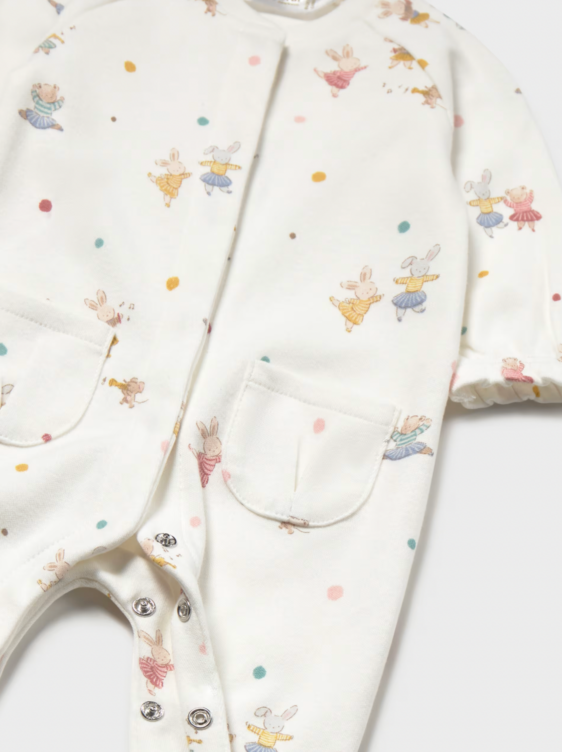 Close-up of a baby romper in off-white with a colorful print of bunnies and small dots, featuring snap closures and front pockets.