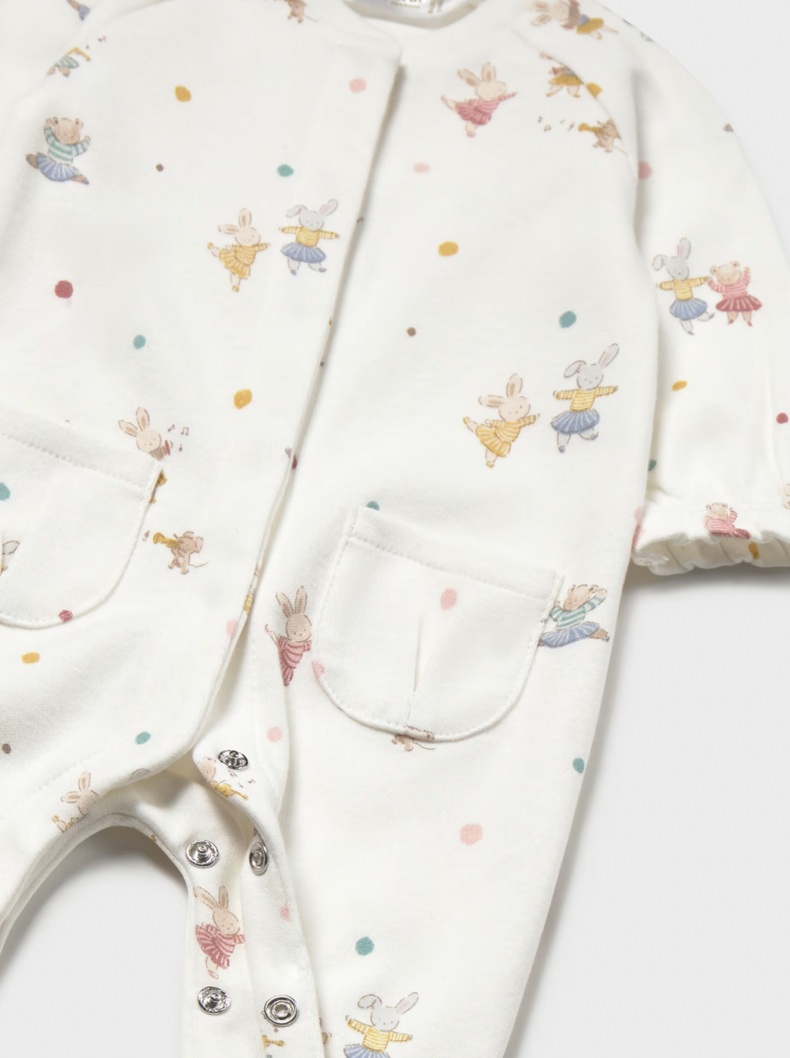 Close-up of a baby romper in off-white with a colorful print of bunnies and small dots, featuring snap closures and front pockets.