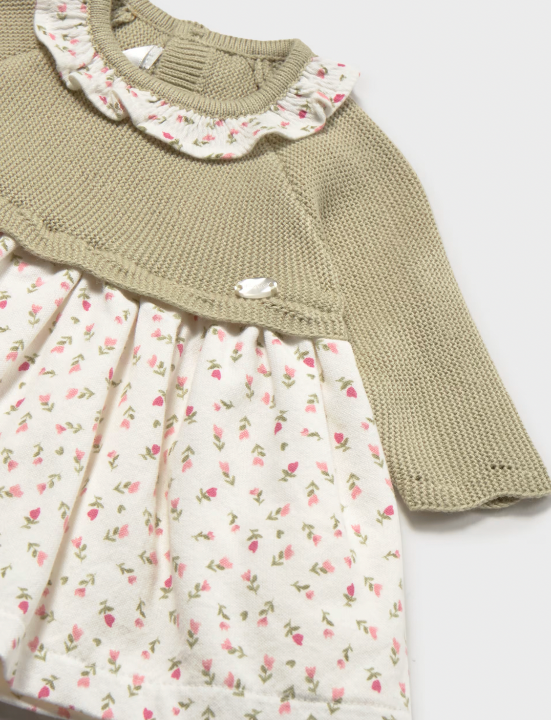 A close-up of a baby girl's dress featuring a textured olive green knit long-sleeve top and a cream-colored skirt with a small pink and green floral print.