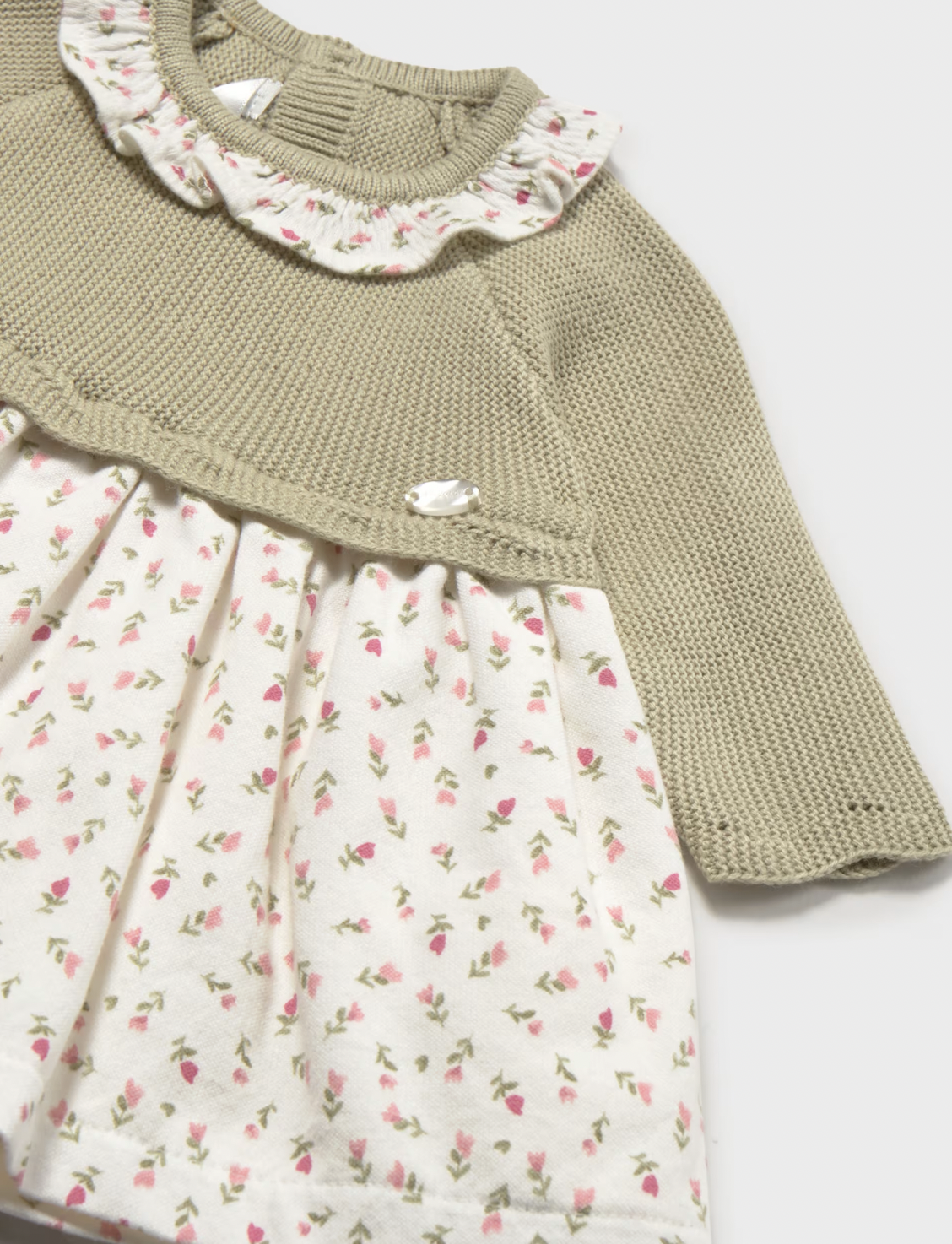 A close-up of a baby girl's dress featuring a textured olive green knit long-sleeve top and a cream-colored skirt with a small pink and green floral print.